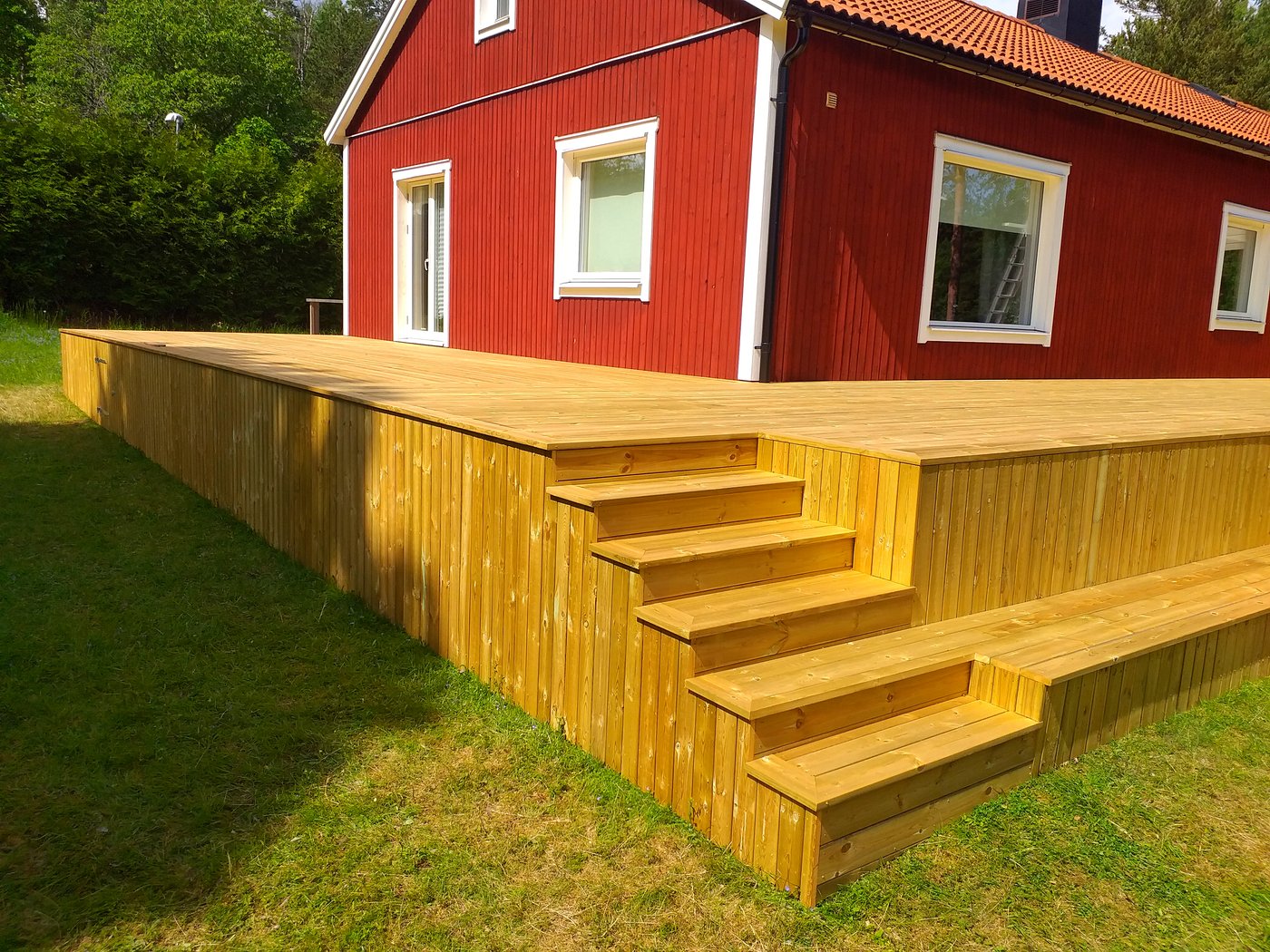 Träaltan med bred trappa vid ett rött hus